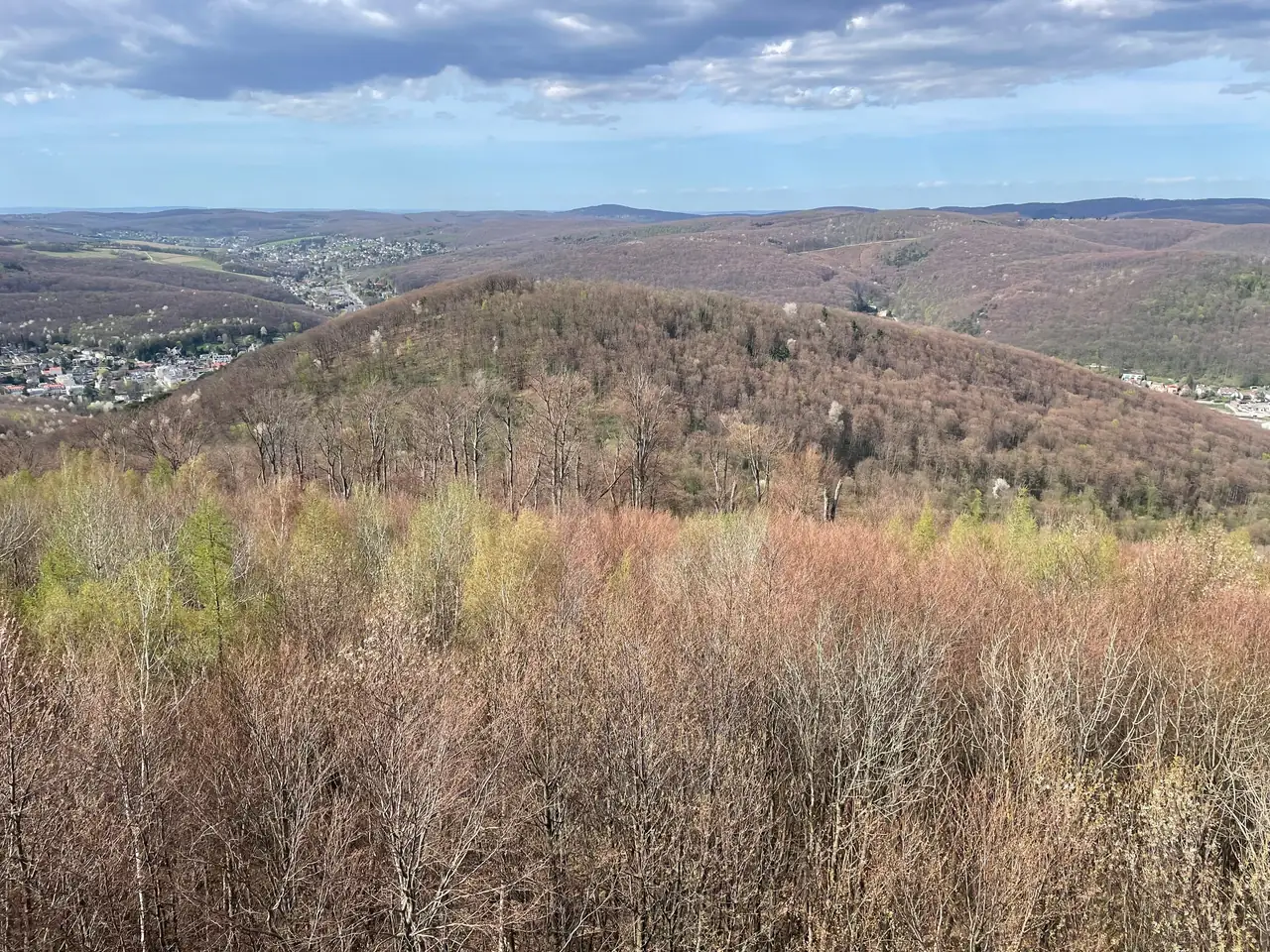 Colinas ondulantes cubiertas de bosque y pueblos cercanos, vistos desde un mirador elevado en primavera.