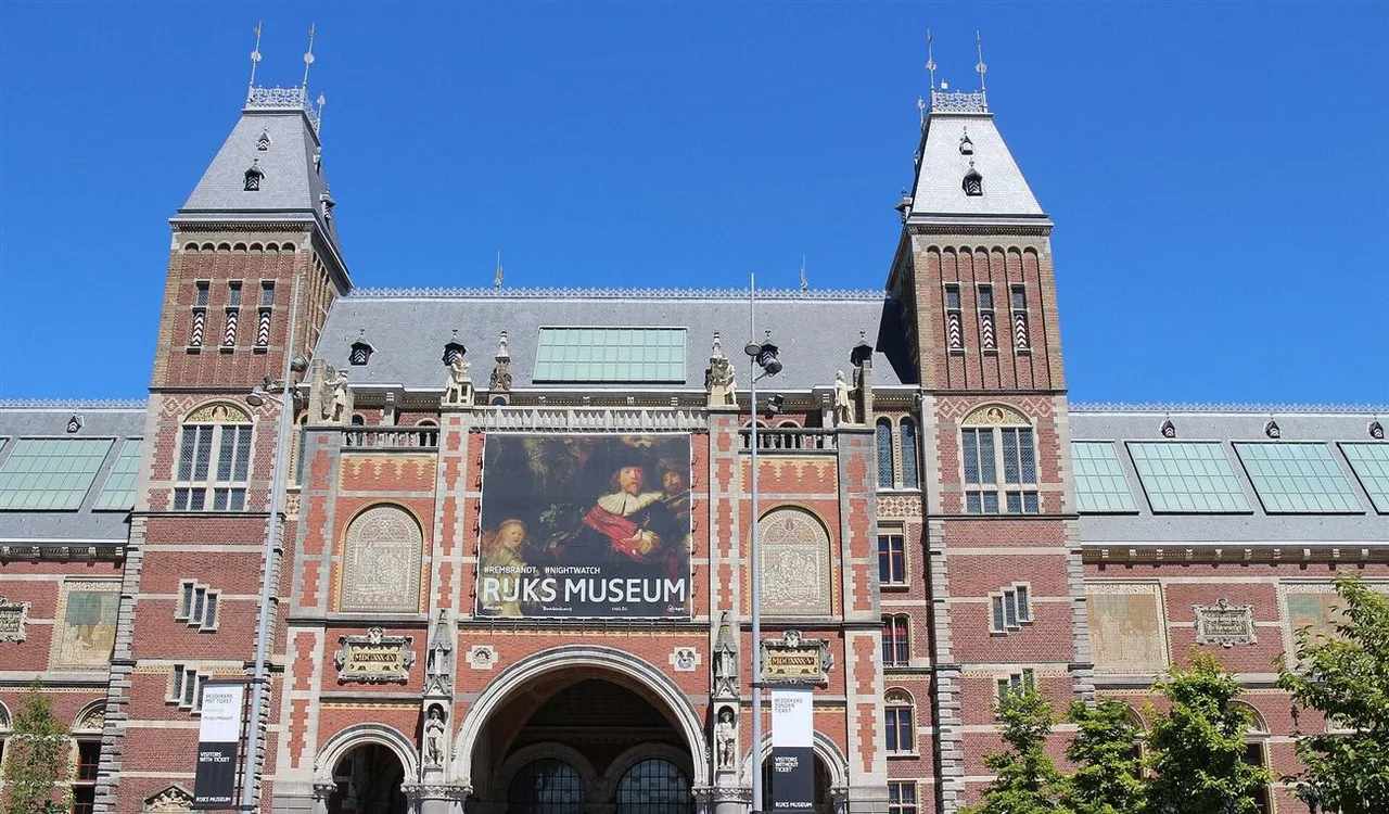 Red brick museum facade with two pointed towers, a large banner above the central arch and a clear blue sky.