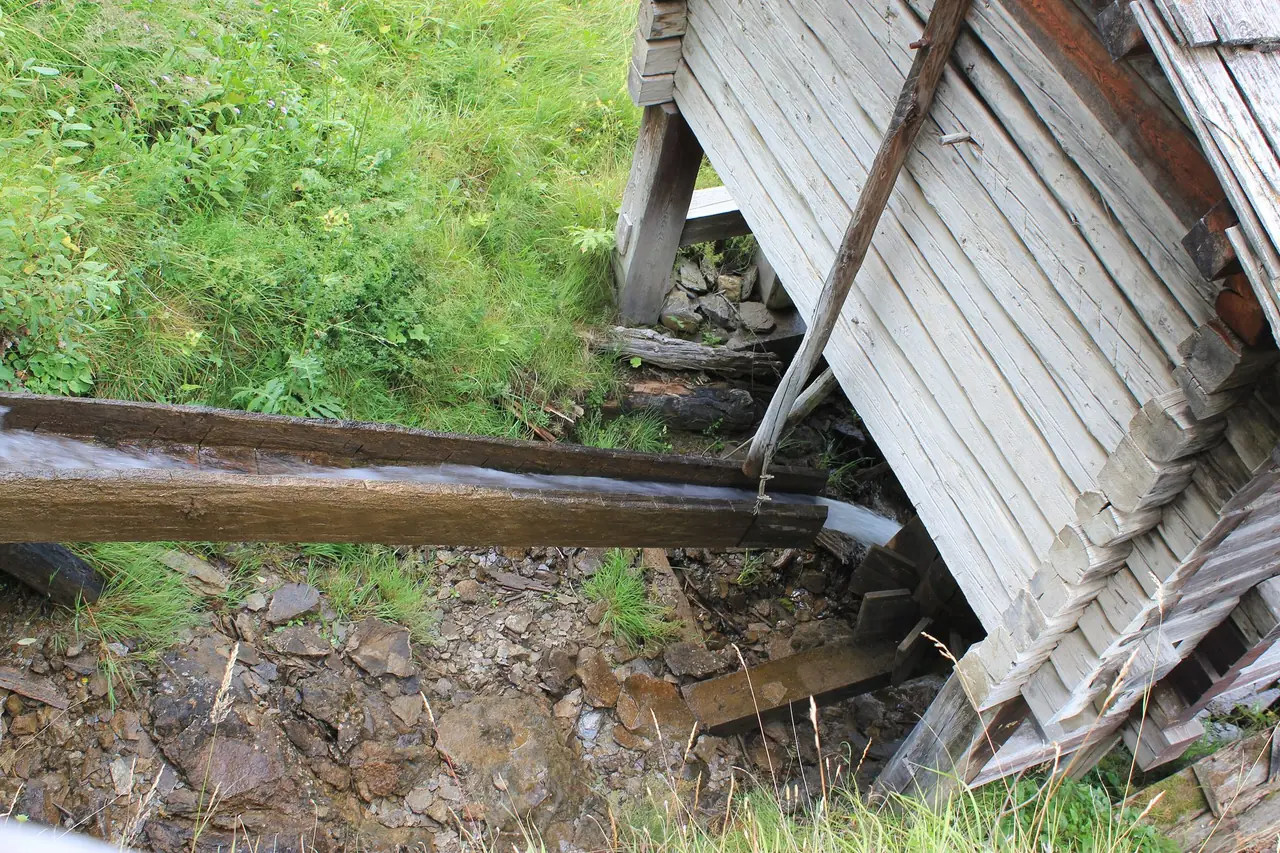 Looking down on a wooden water channel running under the raised timber floor of a mill in Apriach