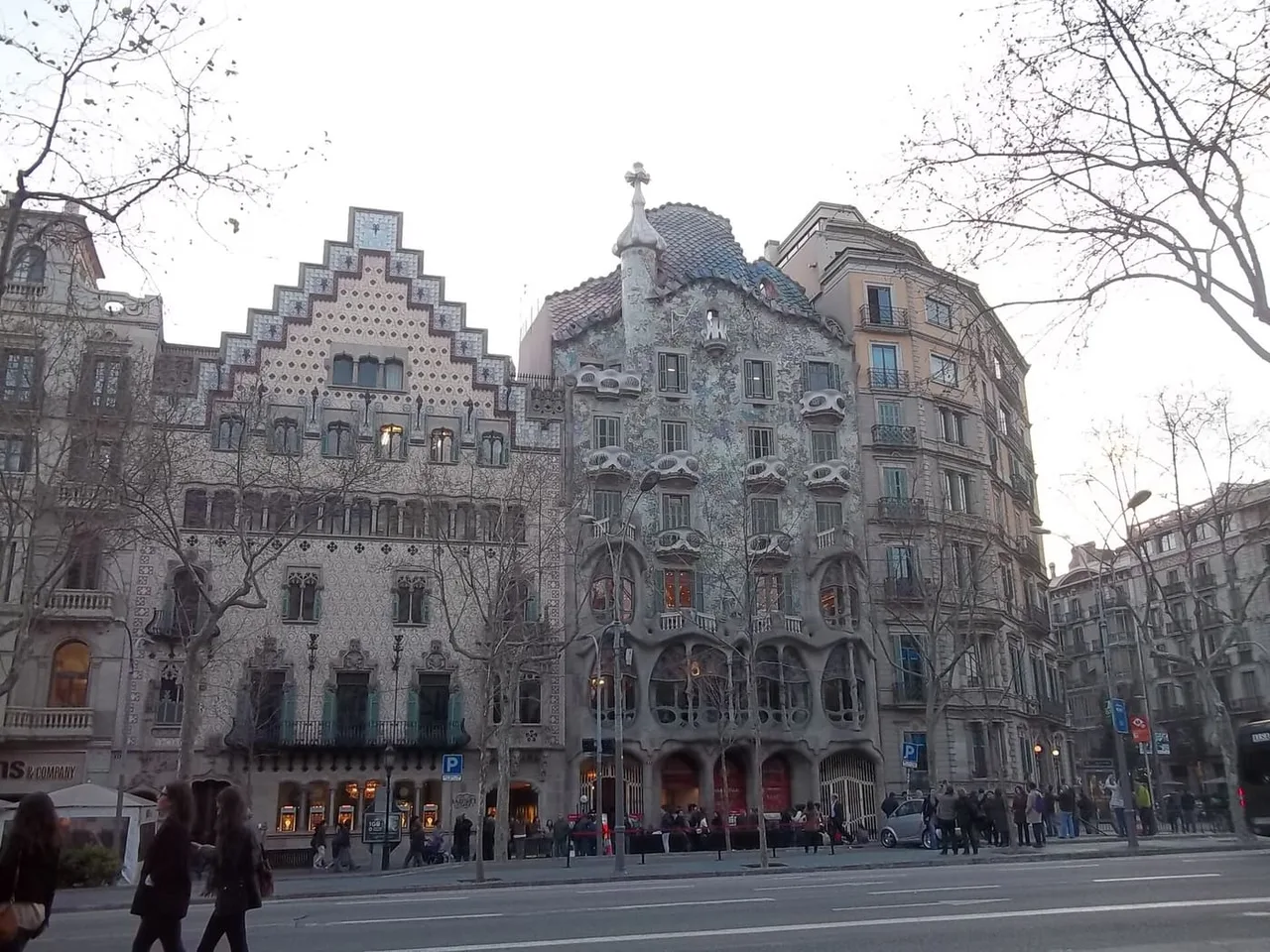 Casa Batlló with its curved, mosaic-covered façade beside the stepped gable of Casa Amatller on a tree-lined Passeig de Gràcia.