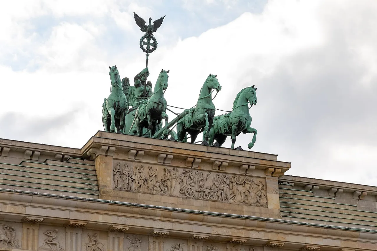 Bronze quadriga with a winged figure and eagle standard on top of the sandstone Brandenburg Gate, above a carved relief frieze.