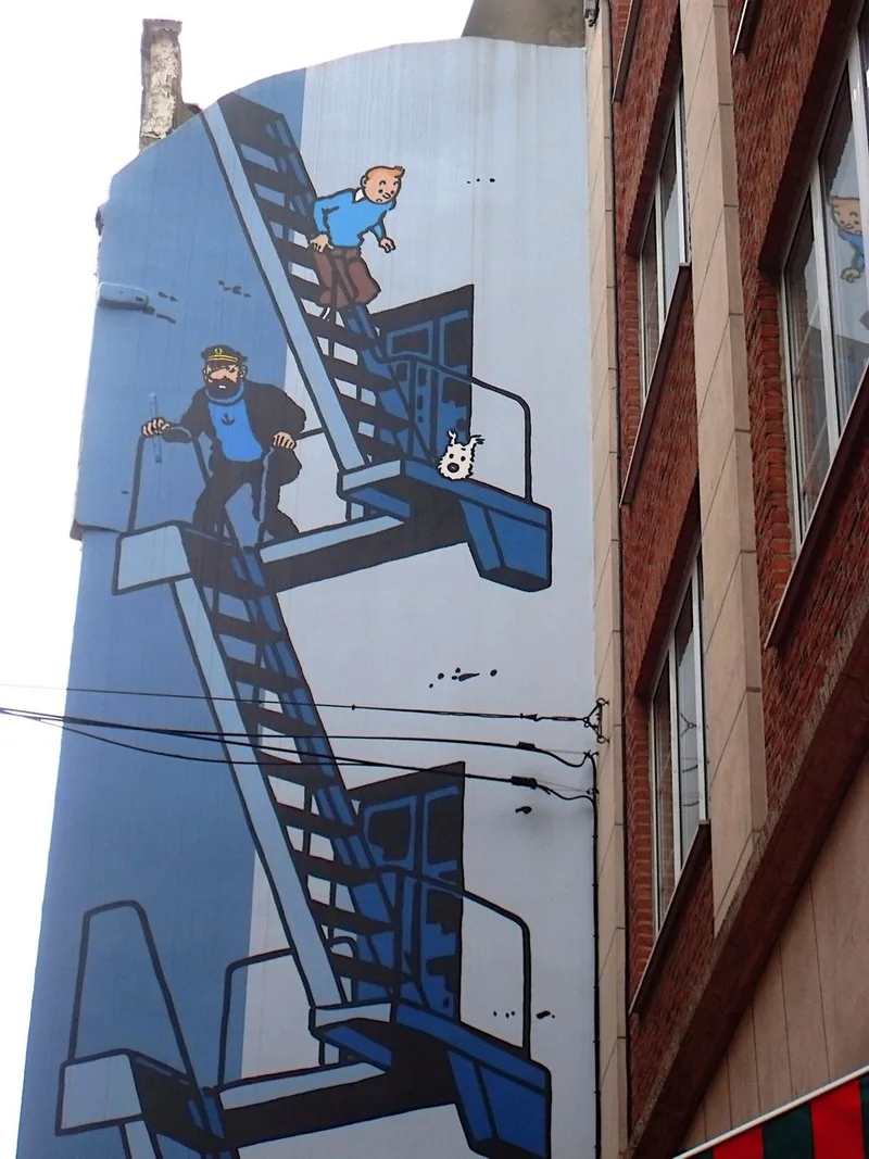 A painted gable wall in blue showing Tintin and Captain Haddock on a fire-escape stairway with the small white dog Snowy, beside a red-brick building.