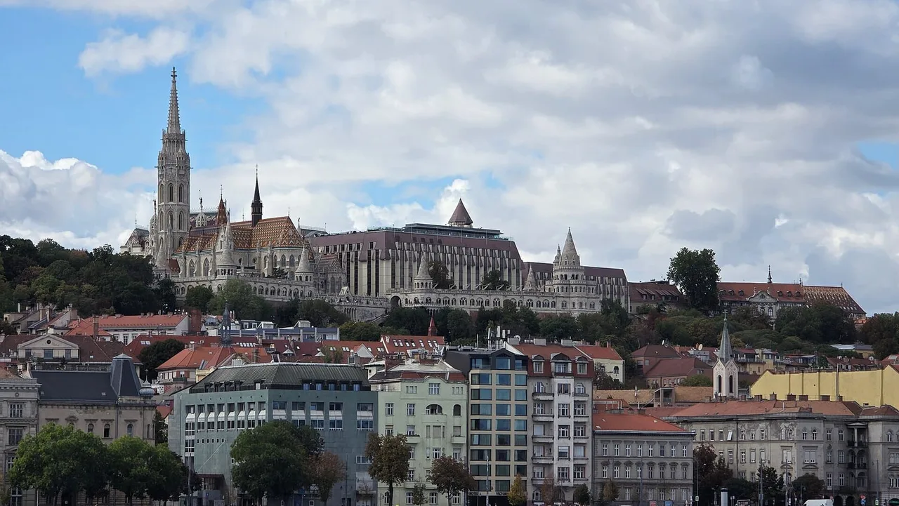 Hillside above city rooftops with the tall Gothic spire and tiled roof of Matthias Church beside the white turrets of the Fisherman's Bastion.