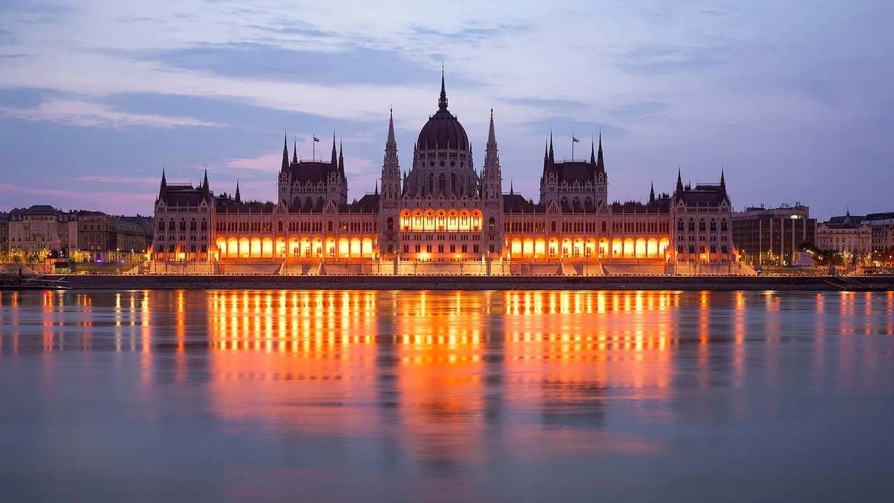 The neo-Gothic Hungarian Parliament Building lit in orange at dusk beside the Danube, reflected in the still water.