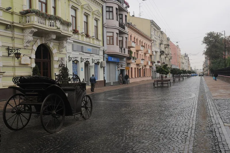 A cobbled stretch of Olha Kobylianska Street lined with pastel-coloured nineteenth-century buildings, with an old carriage at left.
