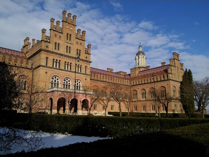 The red-brick Residence of the Metropolitans with stepped gables, a patterned tile roof and a small tower, seen across a hedge and park.