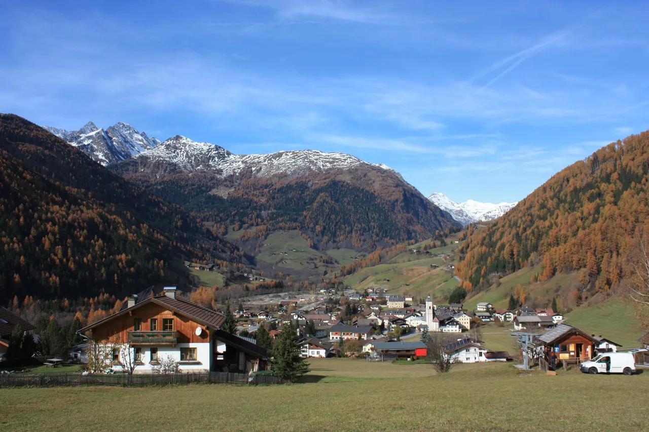 View over the village of Döllach in the Mölltal with a church tower, larch forest in autumn colours and snow-covered peaks