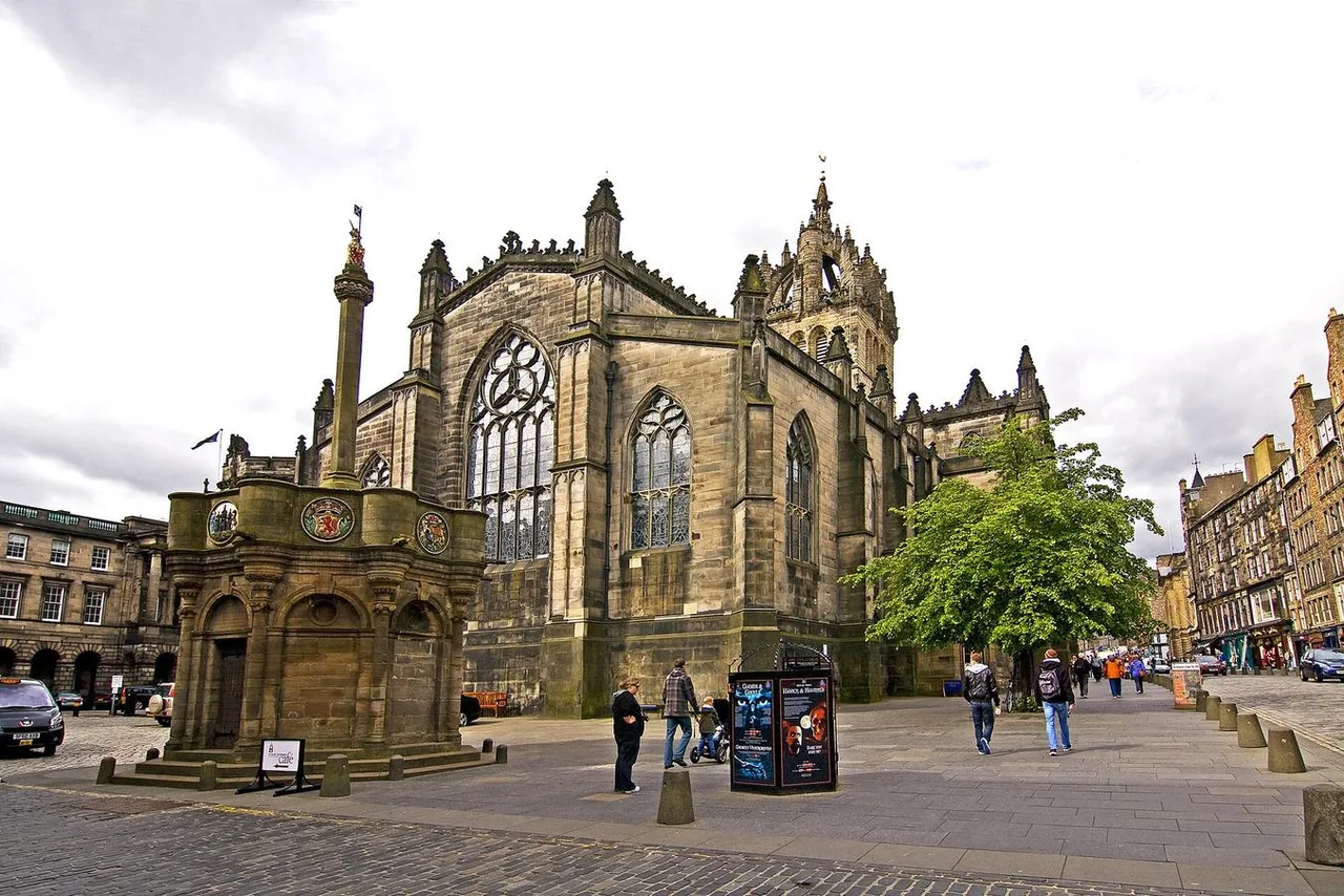 The Mercat Cross beside the dark stone crown tower and large Gothic window of St Giles' Cathedral on the Royal Mile.