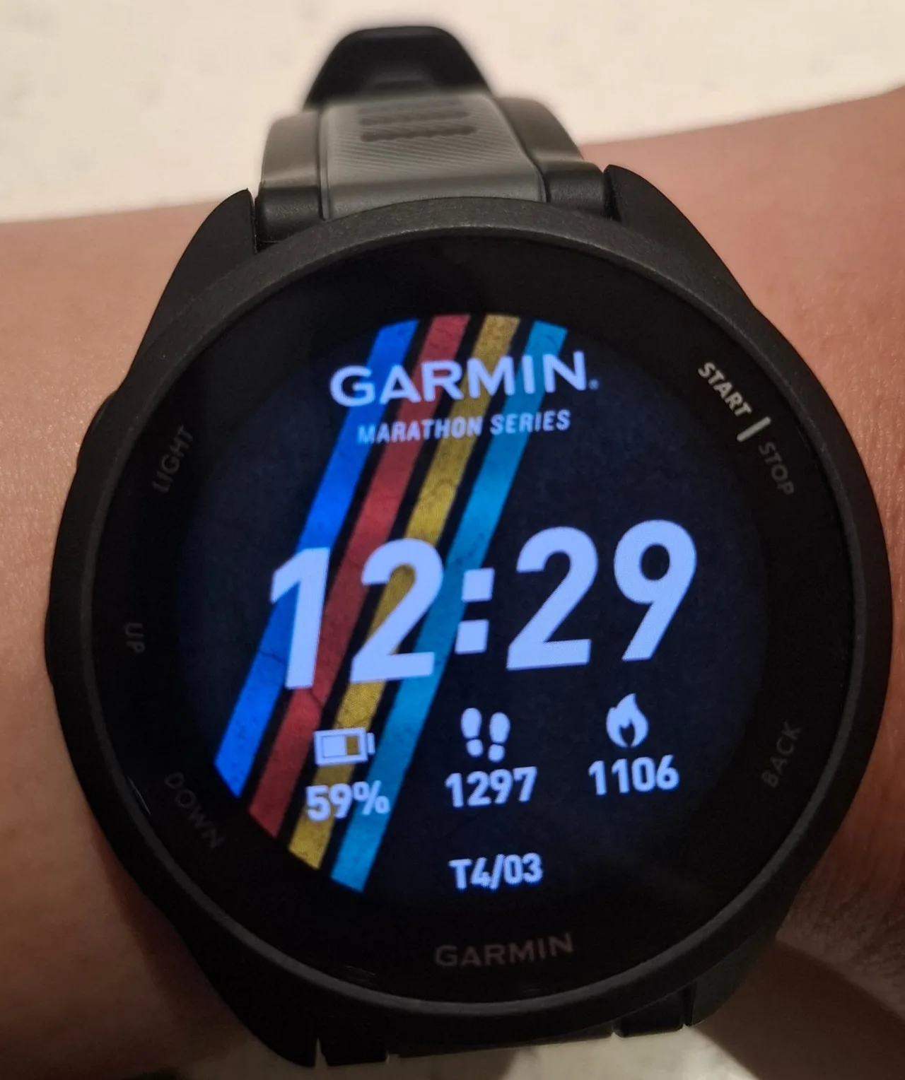 A black Garmin Forerunner 165 on a wrist, with a Marathon Series watch face of blue, red and yellow diagonal stripes.