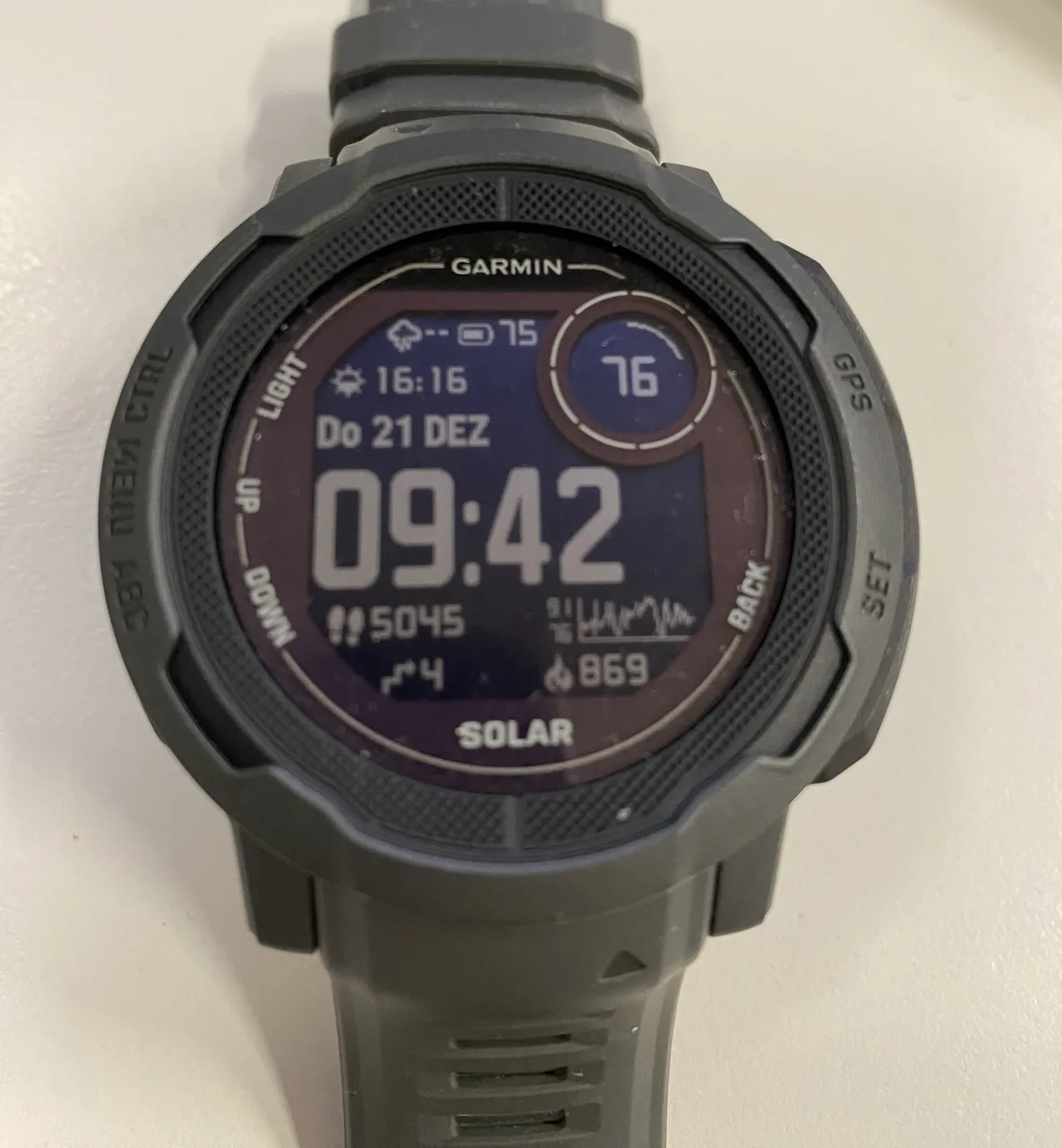 Close-up of a dark grey Garmin Instinct 2 Solar with a digital watch face, the word Solar below the display and a thick rugged bezel.
