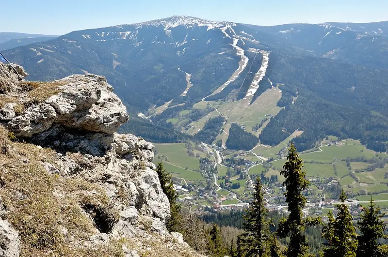 View from a rocky edge on the Kampalpe across the valley to the Stuhleck, with pale ski runs on the forested slope and the village below