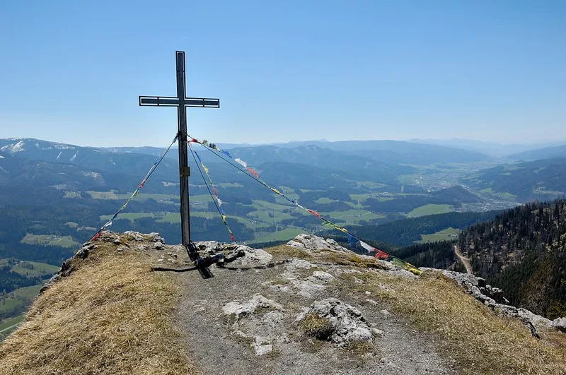 Metal summit cross on the Kampalpe with colourful flags tied to it and a wide view over the valleys