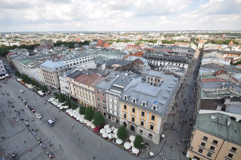 Aerial view of the Old Town rooftops and the Main Market Square, with cafe umbrellas along one side and a long street running off to the right.