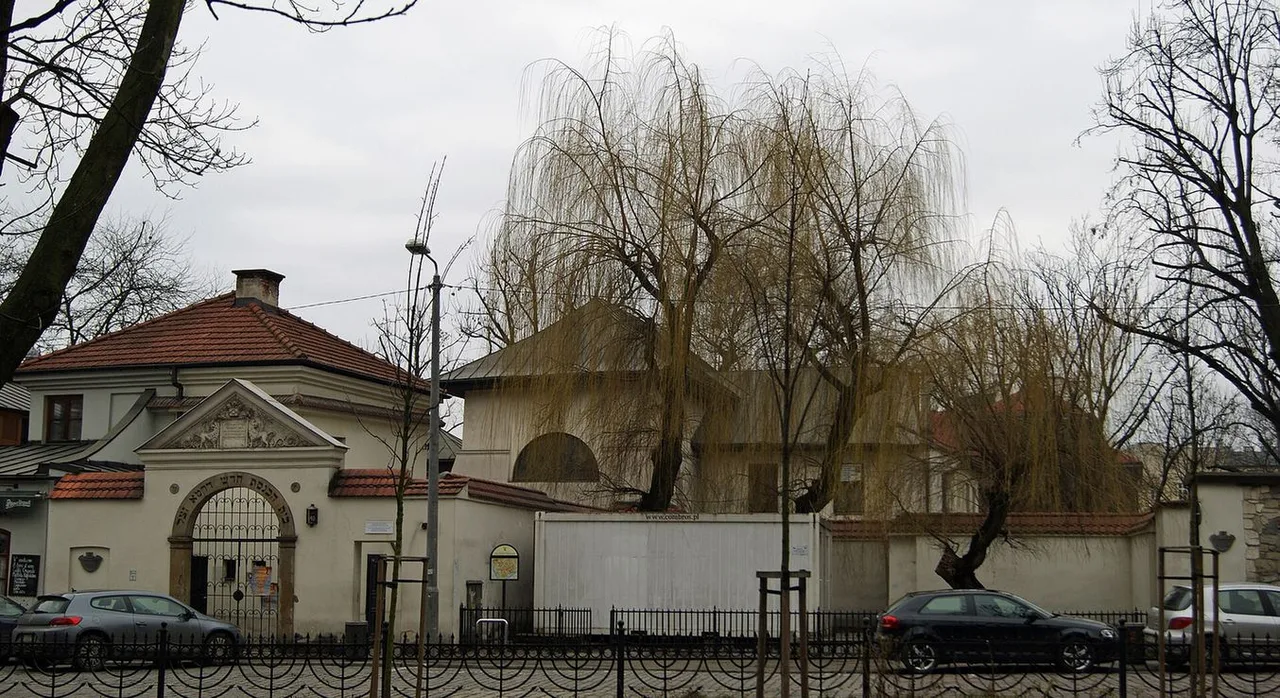 Stone walls and a Renaissance gateway beside the Remuh Synagogue on Szeroka Street, with bare willow trees and parked cars in front.