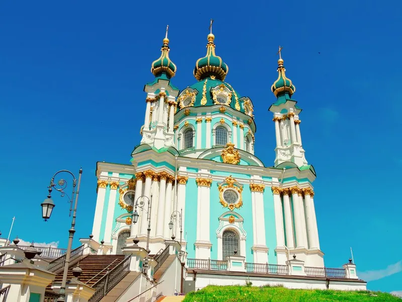 The turquoise and white Baroque Saint Andrew's Church with gilded details and green domes against a blue sky.