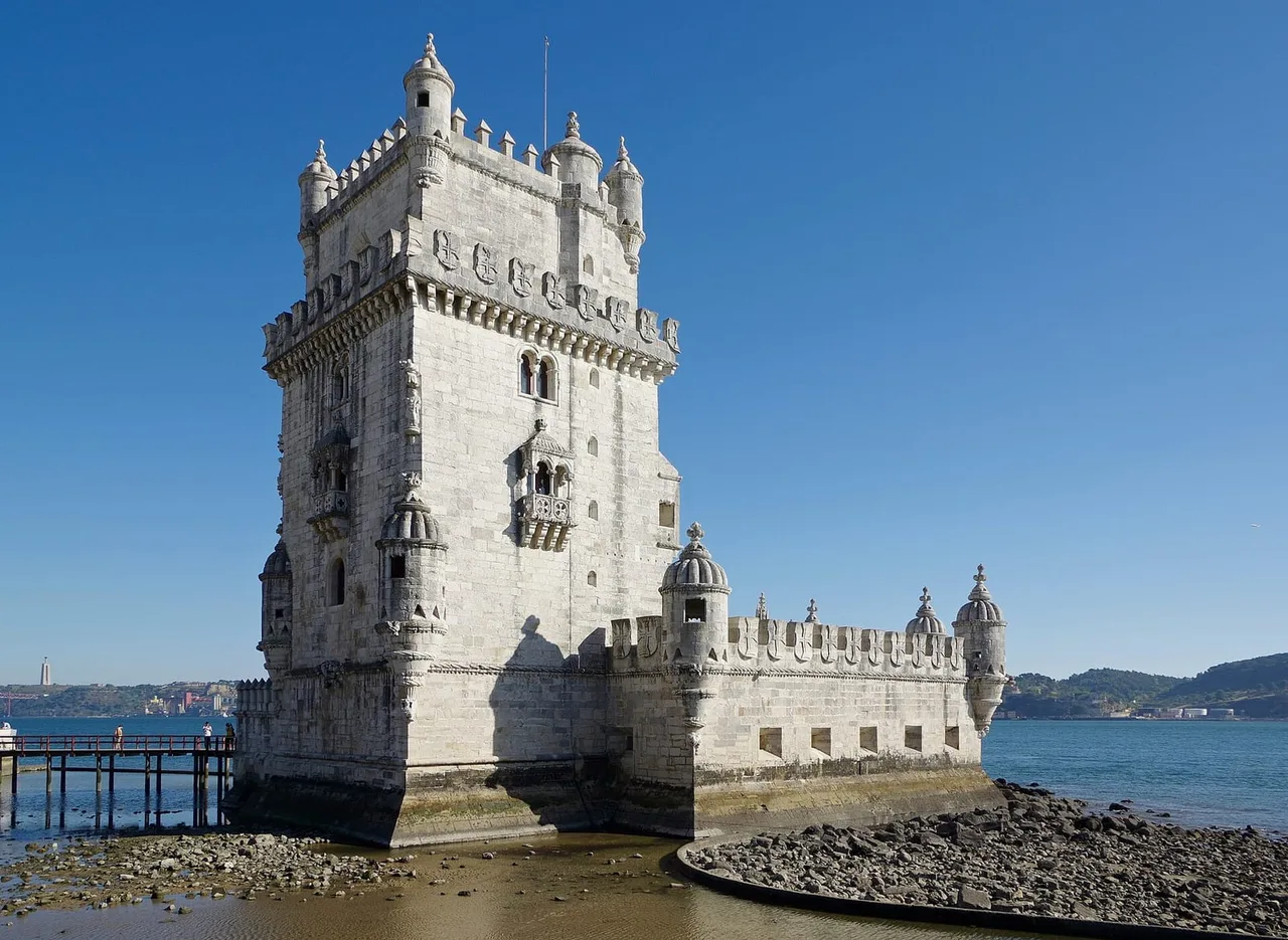 The pale limestone Tower of Belém with turrets and battlements standing at the edge of the Tagus under a clear blue sky.