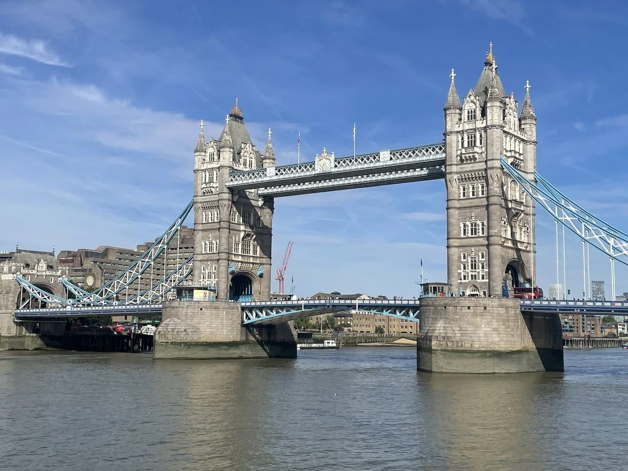 Tower Bridge with its two Gothic towers and blue suspension girders spanning the Thames on a sunny day.