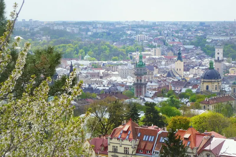 Lviv old town seen from a hill, with church towers and a green dome among red tiled roofs and blossoming branches in the foreground.