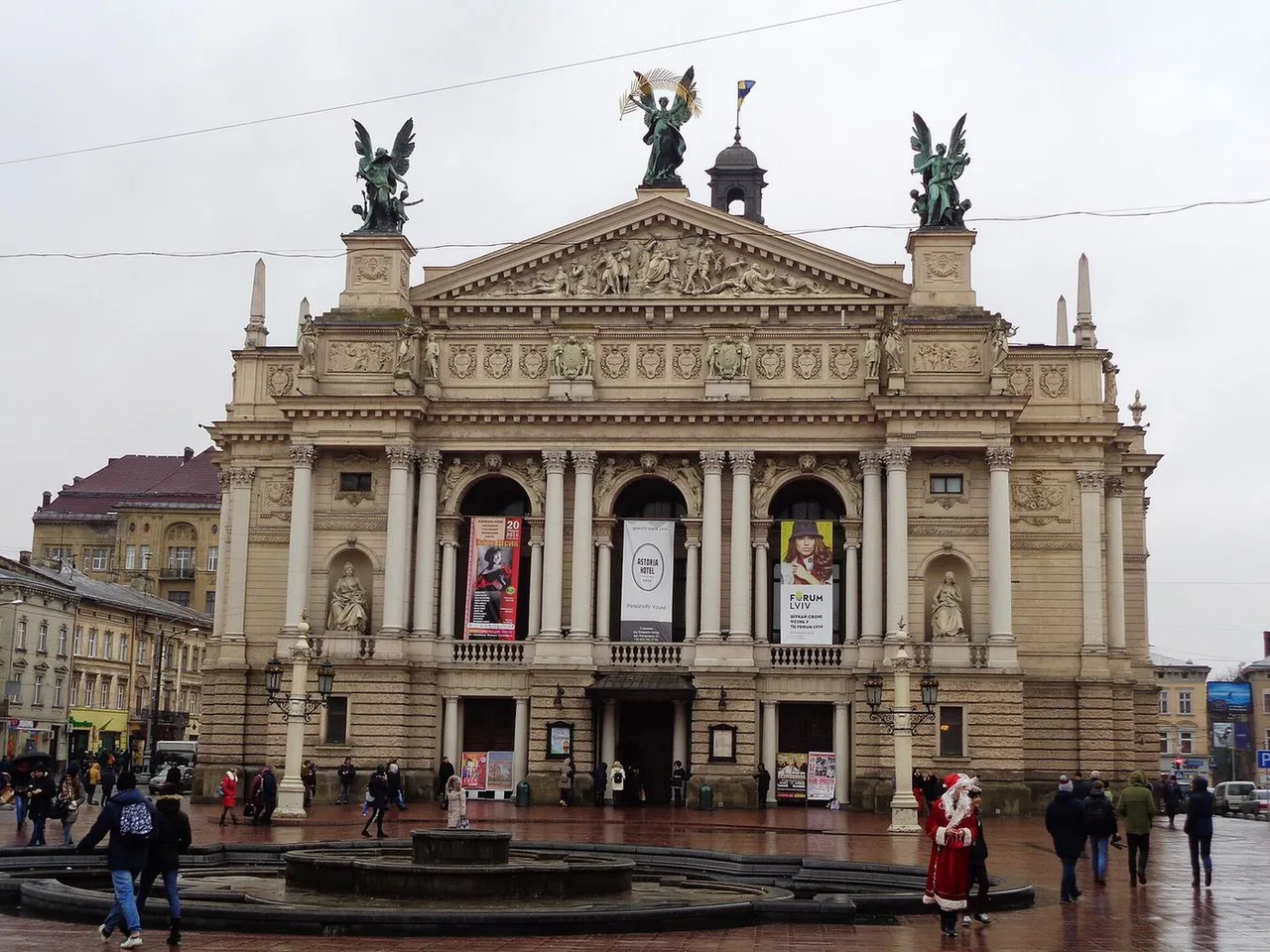 The neoclassical front of the Lviv Opera House with a pediment, columns and bronze figures on the roof, seen from the plaza in front.