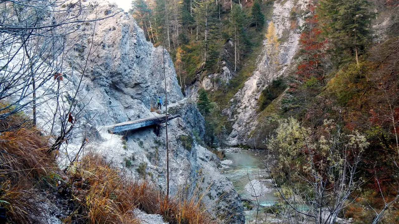A narrow path runs along a pale limestone wall above the stream in the upper Ötschergraben, with autumn-coloured trees on the far slope.