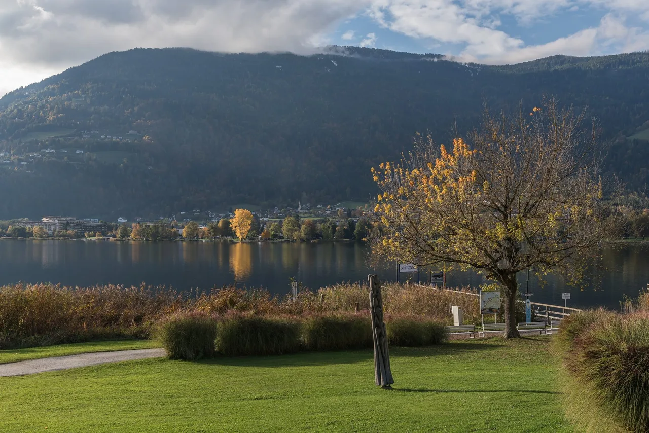 Autumn view across Lake Ossiach from the shore at Ossiach, with a boat jetty and the forested slopes of the Gerlitzen massif