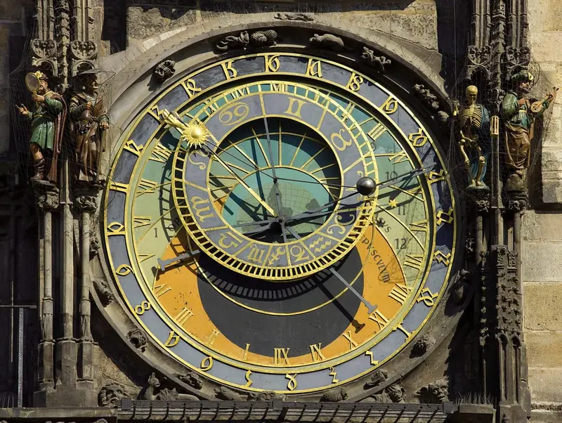 Dial of the Prague astronomical clock with gold zodiac ring and Roman numerals, flanked by painted figures including a skeleton.