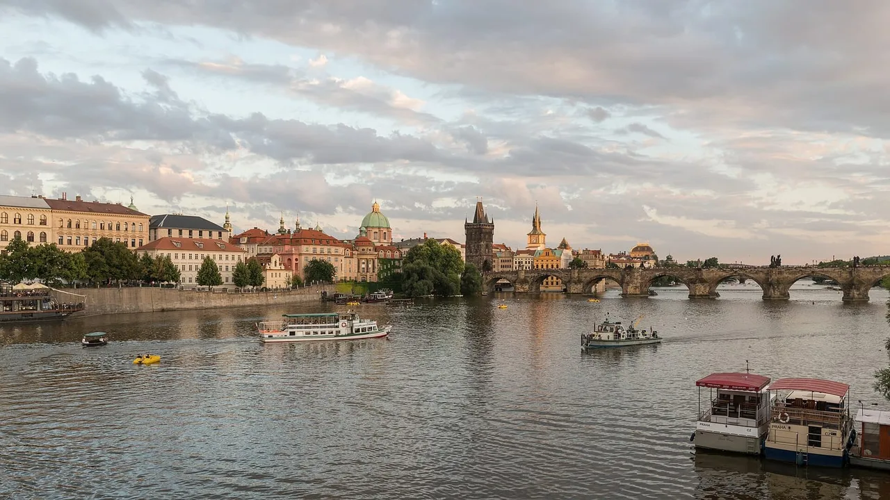 Stone Charles Bridge with its Gothic Old Town Bridge Tower crossing the Vltava, with river boats in the foreground at dusk.