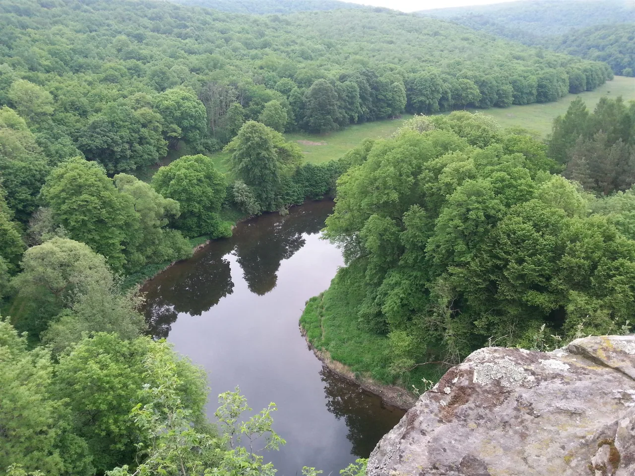 View from a rock outcrop over a wooded valley with the Thaya river curving through a meander.