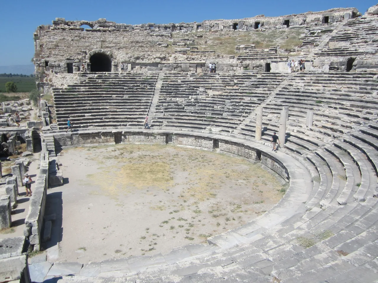 The large semicircular seating of the ancient theatre at Miletus with stone stairways and a plain in the distance