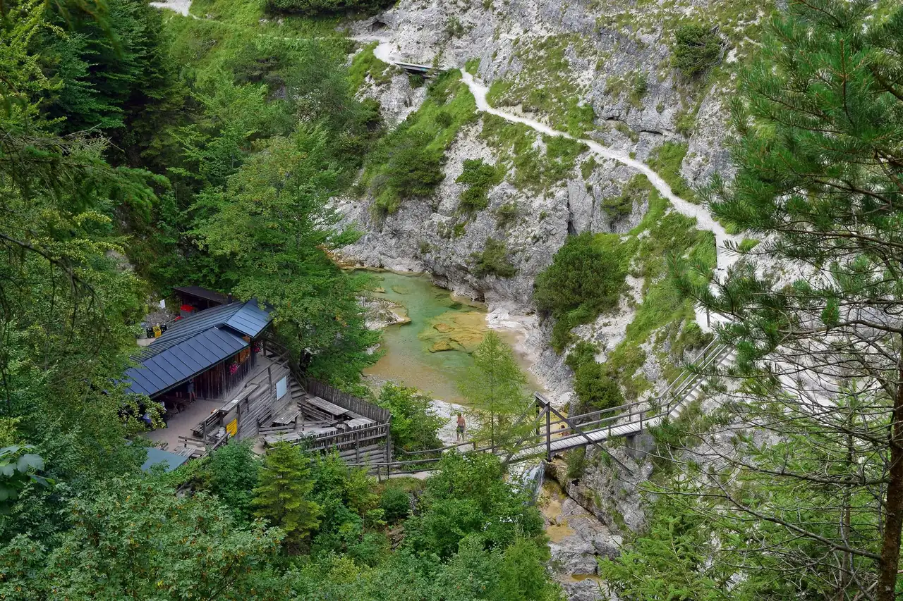The Ötscherbach with clear green water in a limestone gorge, a path on the rock slope above it and the roof of the Ötscherhias hut beside a footbridge.